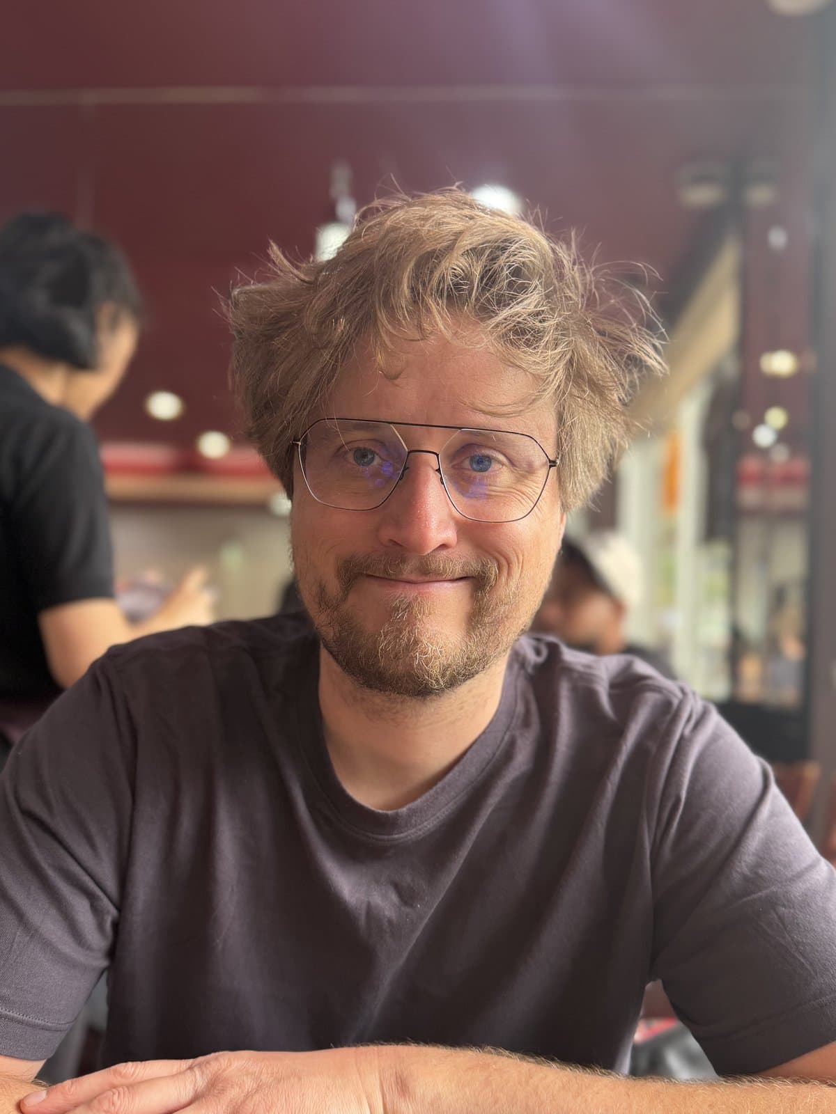 Ian Muirhead, smiling at a café table in a grey t-shirt and glasses